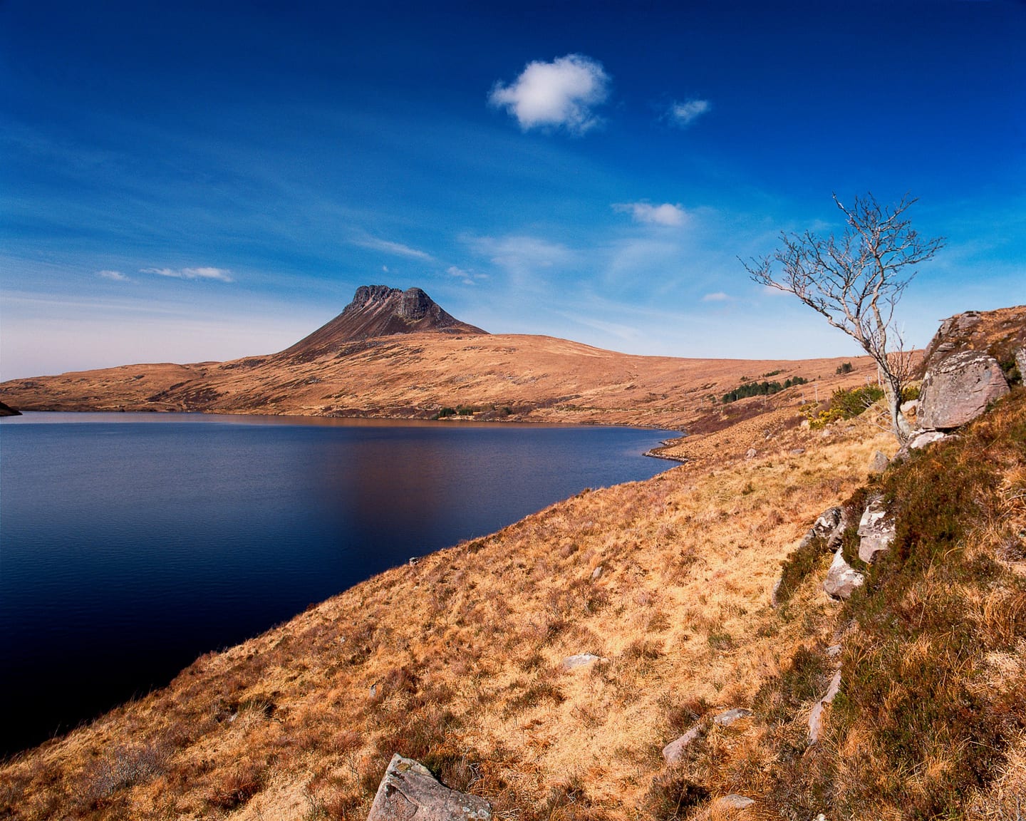 A distinctive rocky peak rises beyond blue water and golden hillsides.