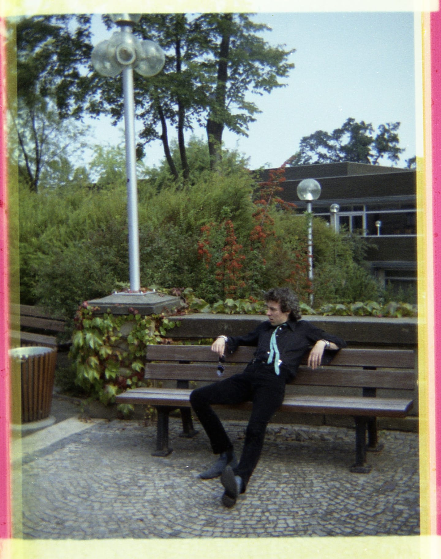 A man in dark clothing sits with his arms stretched along a wooden bench.