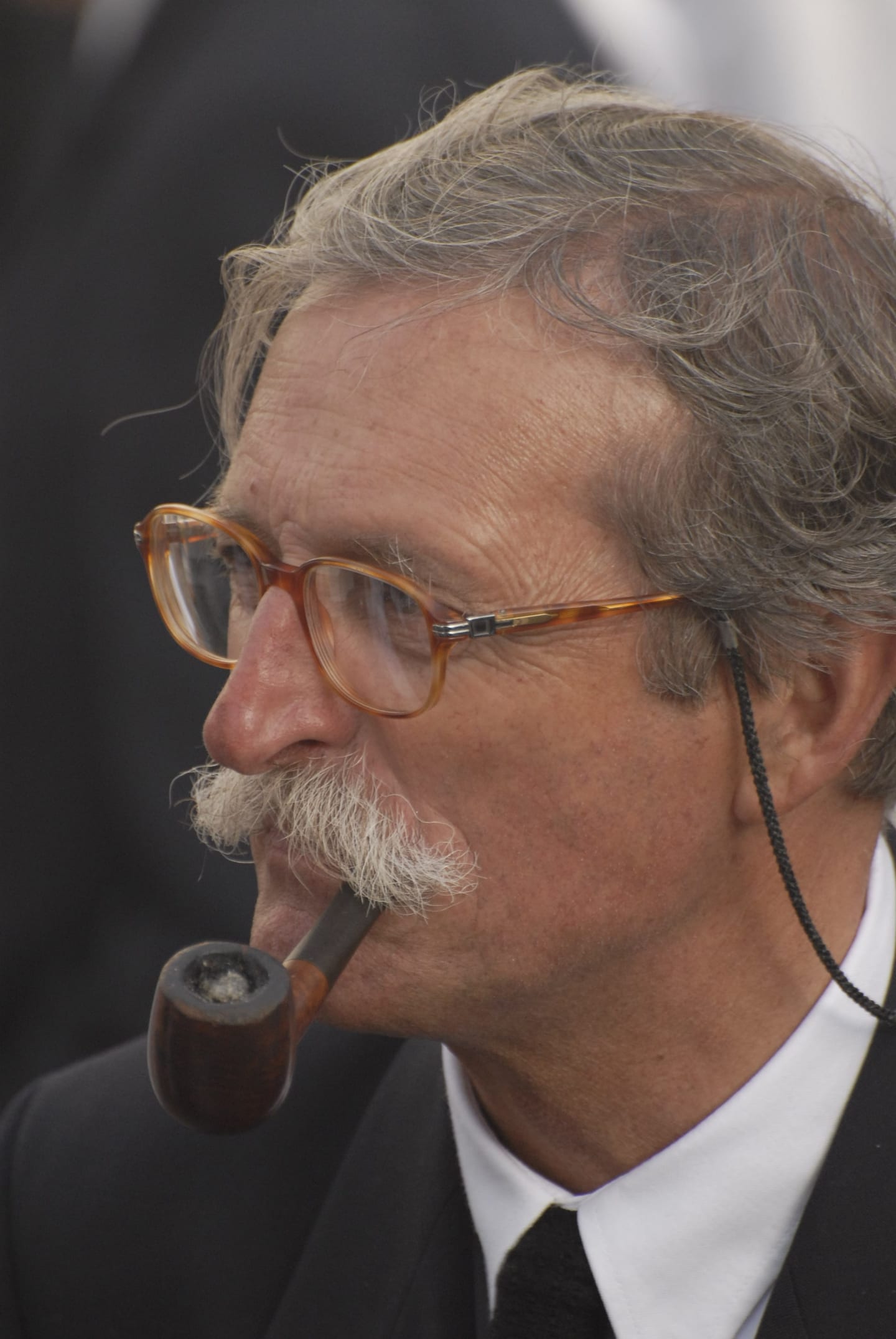 A man with glasses and a moustache smokes a pipe in profile.
