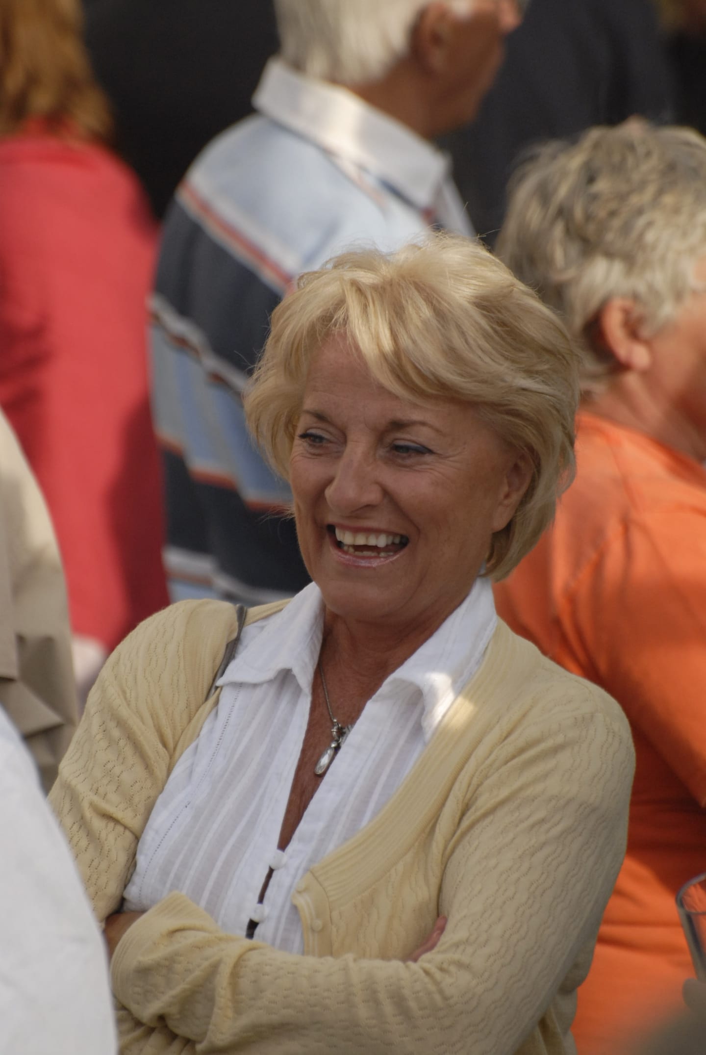 A smiling woman in a cream cardigan at an outdoor gathering.