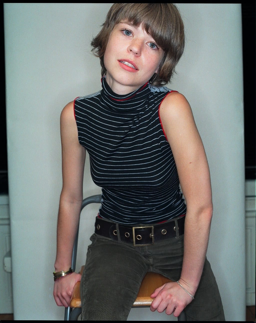A woman with short hair sits on a chair wearing a striped sleeveless top.